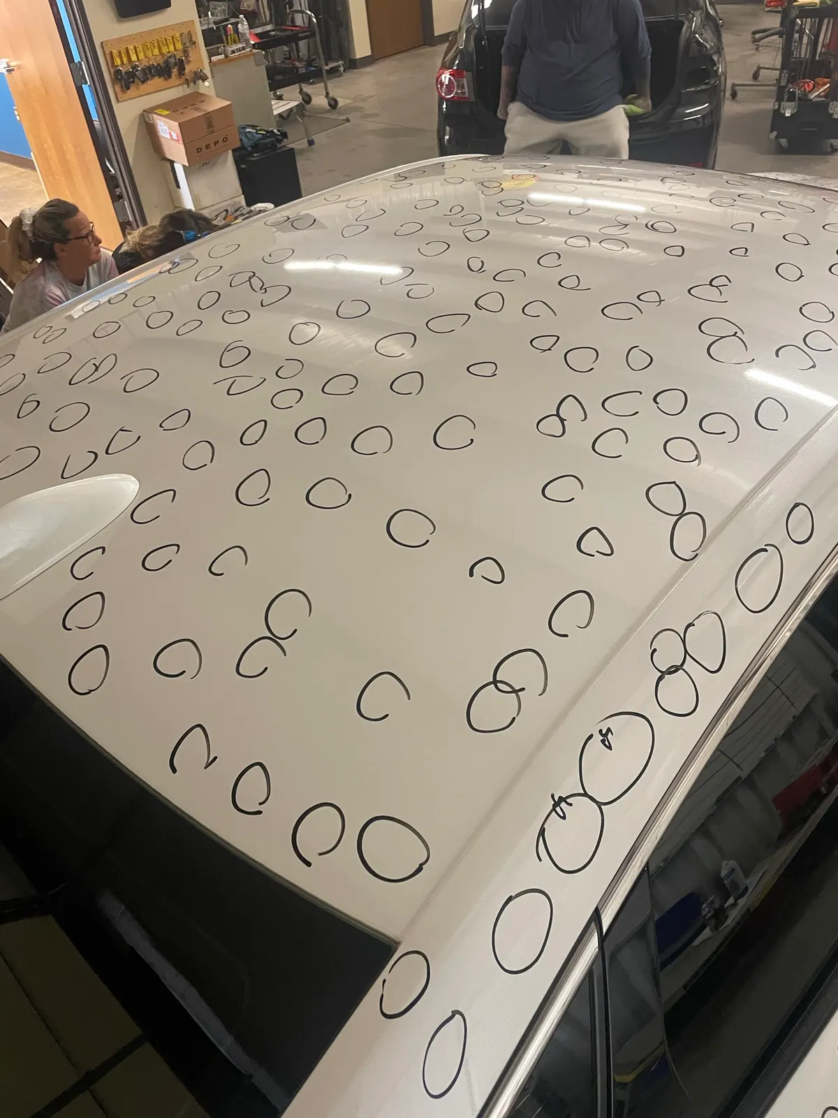 White vehicle roof with over 200 individual hail dents circled in black marker for damage documentation