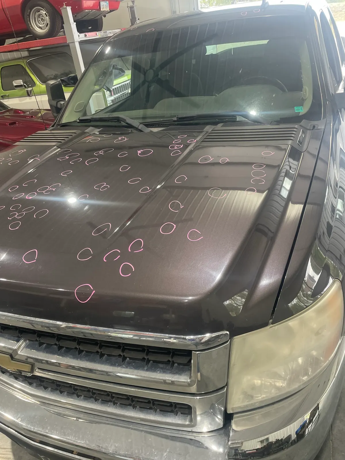 Dark brown Chevrolet Silverado hood with ~60 hail dents circled in pink marker for adjuster documentation