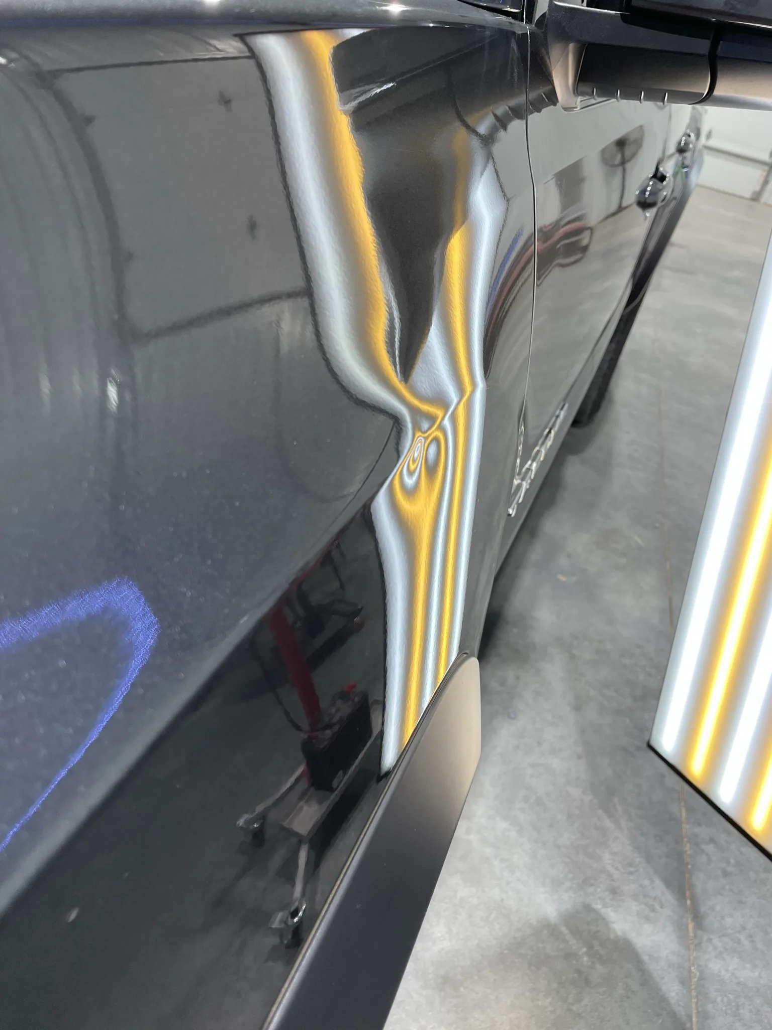 LED line board revealing hail dents on dark vehicle hood at Hail Solutions Olathe