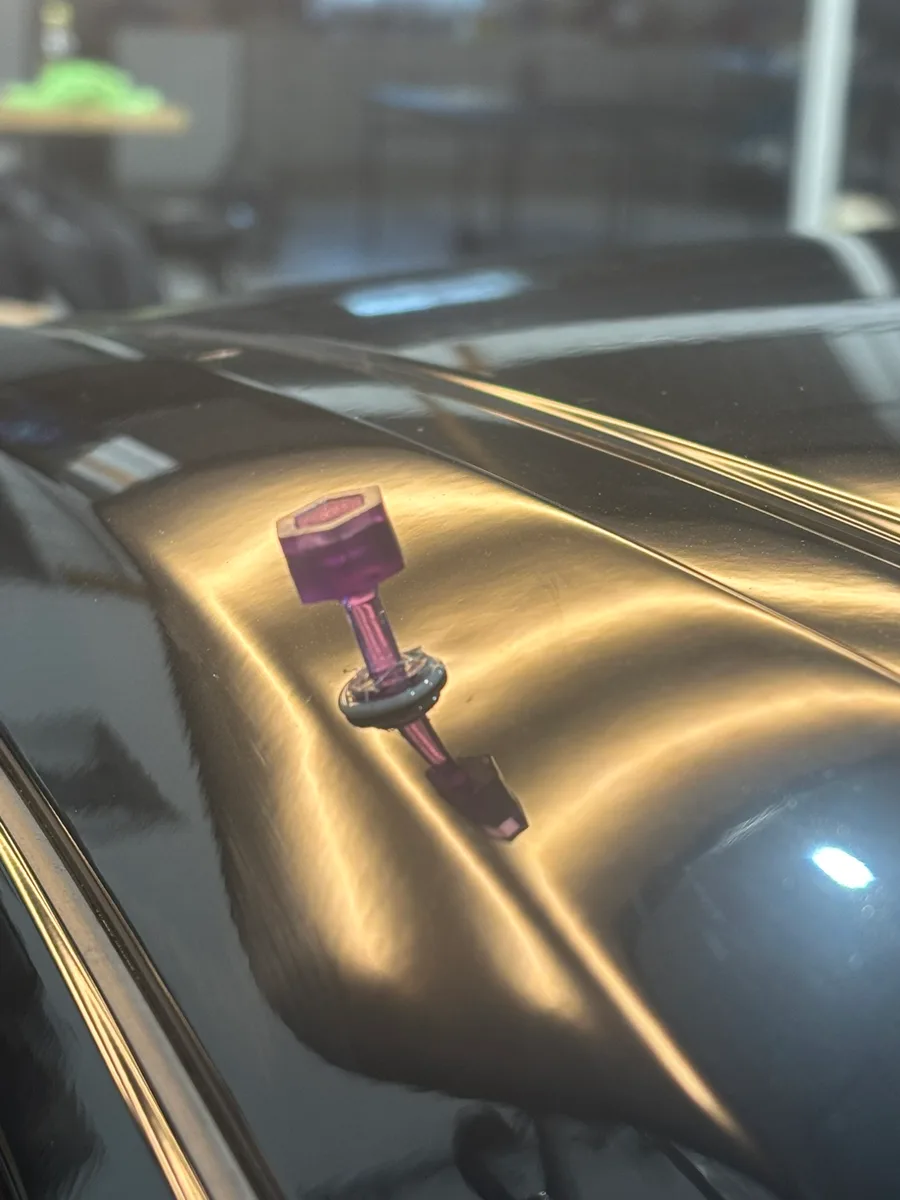 Paintless dent repair in progress with a glue-pull tab on a black vehicle panel