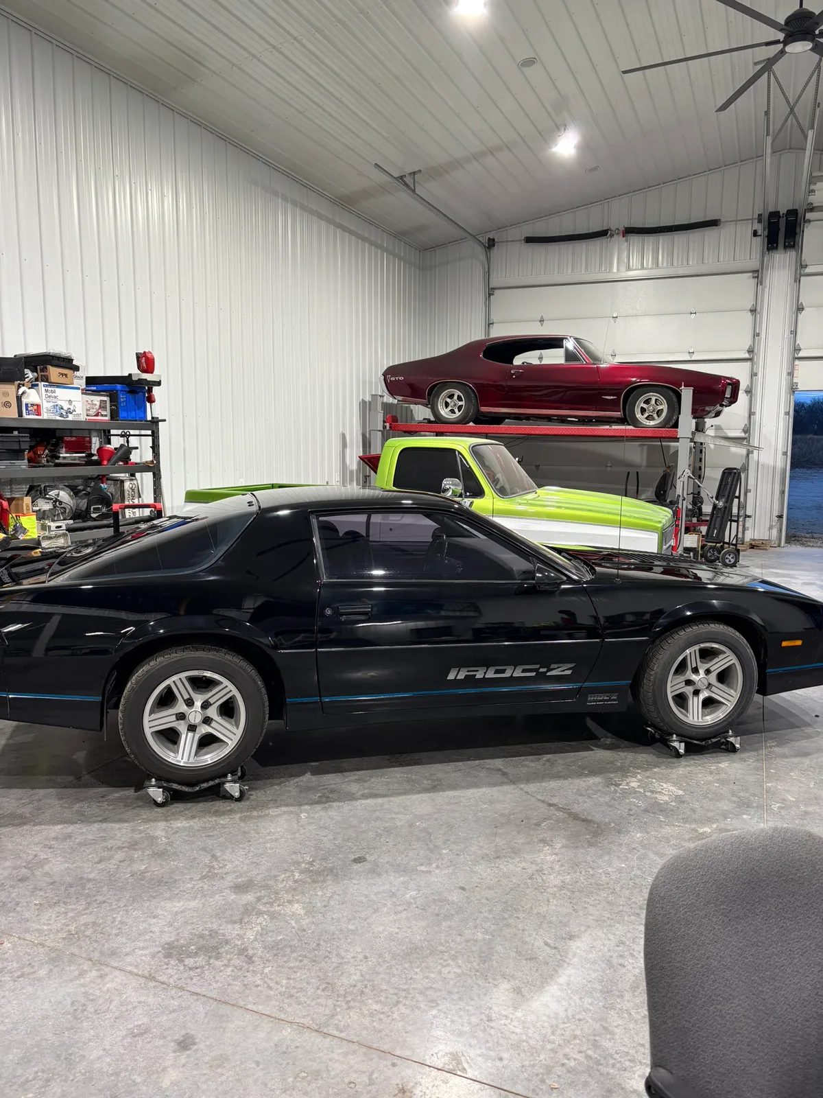 Hail Solutions shop interior showing a black Camaro IROC-Z and two classic cars on lifts in the multi-bay facility in Olathe Kansas